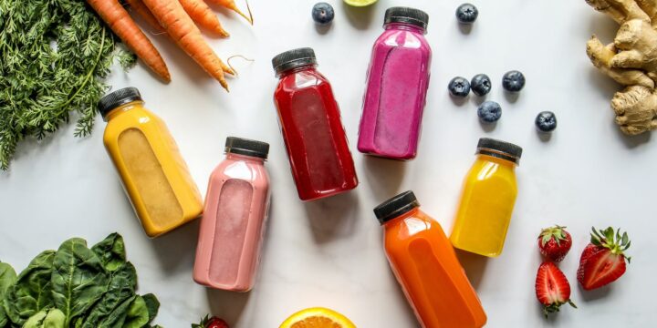 Colorful Bottles with Smoothies Beside Carrots, Ginger, Leaves and Berries