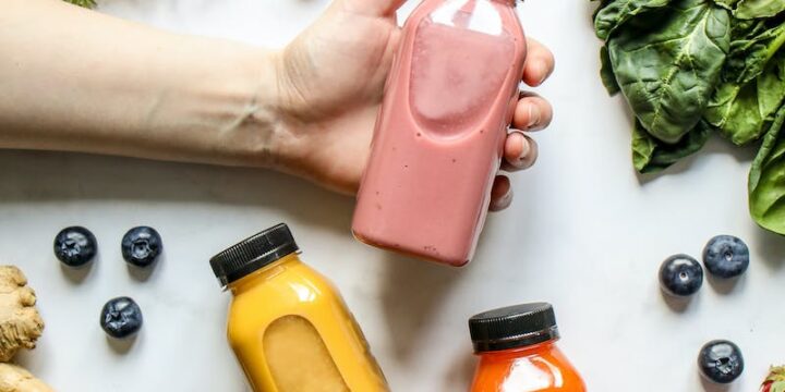 Person Holding Bottle of Smoothie Beside Green Leaves, Carrots and Berries