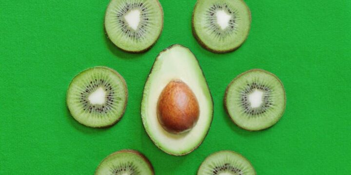 Top view of halved fresh avocado placed on green table with slices of ripe kiwi