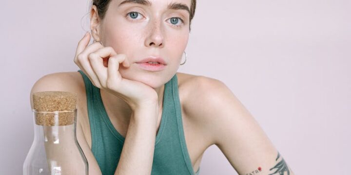 Woman in Green Tank Top Sitting Beside Table With Drinking Glass and Fresh Vegetables