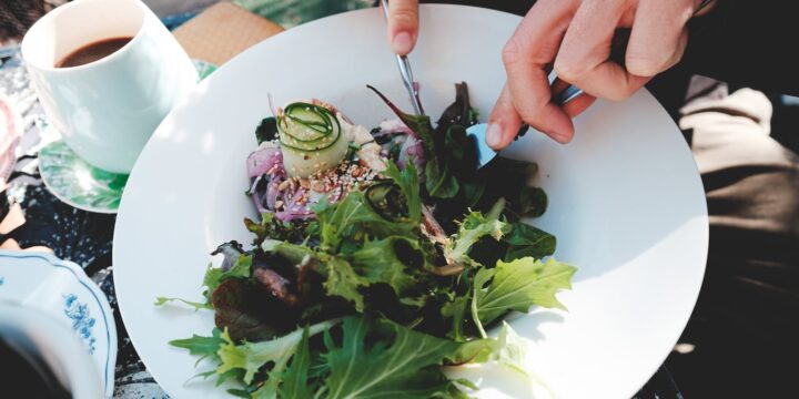 High angle crop anonymous male with cutlery eating tasty mix leaves salads in outdoor restaurant on sunny weather