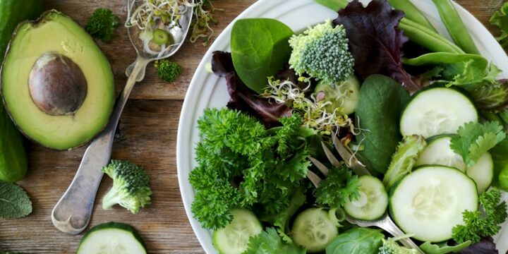 sliced broccoli and cucumber on plate with gray stainless steel fork near green bell pepper, snowpea, and avocado fruit